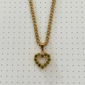 Detail of gold-plated heart pendant necklace with green crystal inlay on dotted background