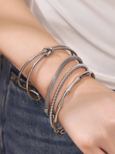 Detail view of silver stainless steel knot and bamboo bangles on a female model wrist