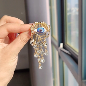 Detail of hand holding a vintage blue eye brooch with tassel chains and crystal decor