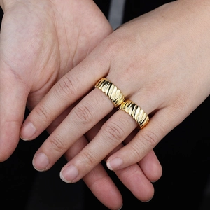 Detail showing two golden rings with wavy croissant texture on a person's hand