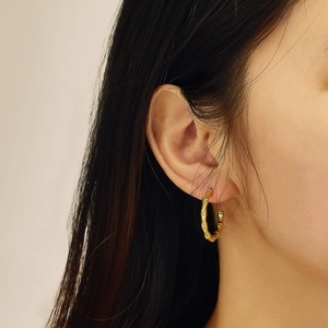 Close-up of a model wearing gold bamboo-textured hoop earrings in stainless steel