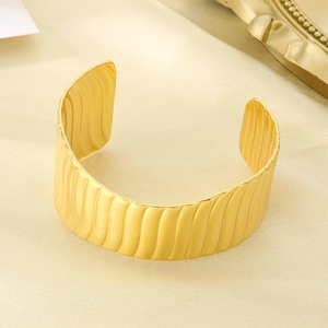 Macro detail of golden wave textured cuff bracelet on elegant silk fabric background