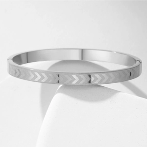Macro shot of silver stainless steel bangle featuring engraved V-shaped arrow patterns