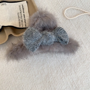 Detail of plush grey faux fur hair claw clip with knit bow on creamy fabric background