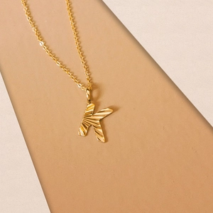 Close-up of golden letter K pendant with sunburst texture on a thin link chain