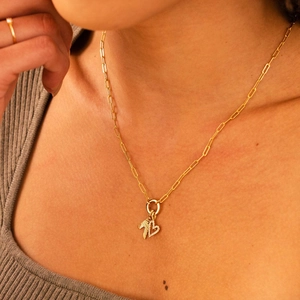 Close-up of gold paperclip chain necklace with leaf and heart pendant on a model