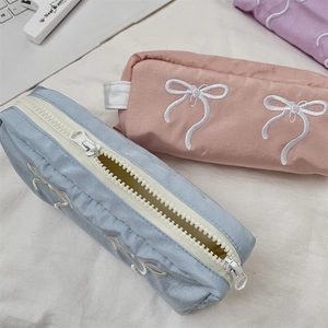 Detailed embroidery of white bows on colorful nylon pencil cases in blue, pink, and purple
