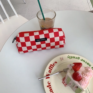 Close-up of red and white checkered corduroy pencil case with a black logo tag
