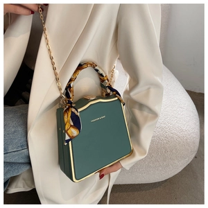 Close-up of retro dark green box bag with gold metal frame and decorative silk scarf handle