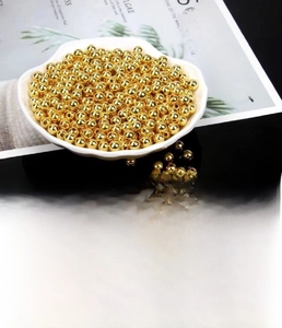 Macro detail of 14k gold-plated solid copper beads displayed in a white decorative bowl