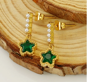 Detailed view of gold star earring with green gemstone and pearls on wooden base