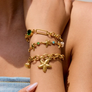 Close-up of gold starfish and shell charm bracelets with green gems on a woman's wrist