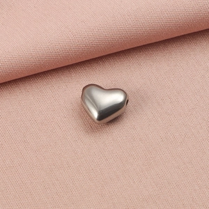Vue macro détaillée d'une perle en forme de cœur argentée sur tissu rose texturé