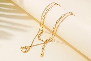 Detail of layered gold stainless steel necklace with heart and abstract face pendants