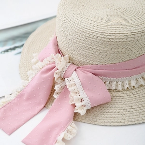 Close-up of beige straw hat with pink polka dot ribbon and white lace trim detail