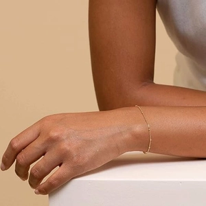 Close-up of a gold bead chain bracelet worn on a woman's wrist in a soft setting
