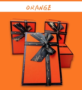 Detailed view of luxury orange gift boxes with black silk ribbons and gold Happy lettering