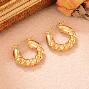 Gros plan détaillé de boucles d'oreilles dorées torsadées en U sur un fond vintage esthétique