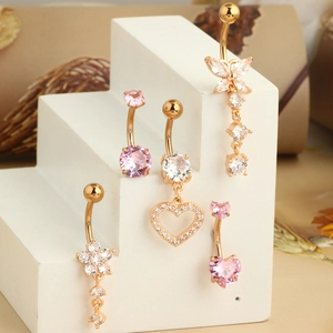 Détail de cinq piercings de nombril or rose avec breloques cœur rose et papillon