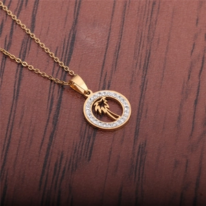 Detail of a gold palm tree pendant necklace featuring white crystal stones on wood background