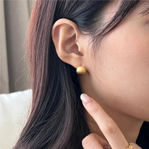Close-up of matte gold sphere stud earring worn by model showing brushed metal texture
