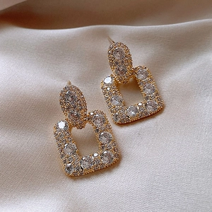 Elegante goldene quadratische Tropfenohrringe mit Kristallen auf Satinhintergrund