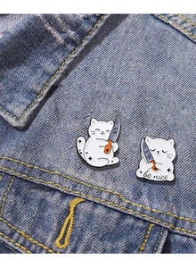 Funny white cat enamel pins with knife on denim jacket, featuring be nice slogan charms