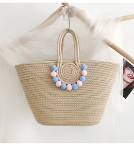 Detailed texture of beige woven tote bag with colorful pom-poms on a wooden hanger