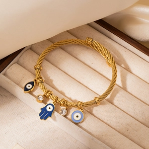 Macro view of gold-plated woven bangle with Hamsa Hand and Evil Eye charms on velvet