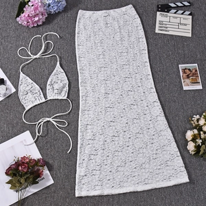 Flat lay of white lace bikini top and matching high-waisted long skirt set with floral decor