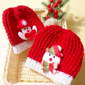Festive red knitted baby hat set with snowman decor and pine branch in a woven basket