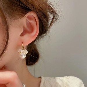 Elegant pearl earrings featuring white flower charms and gold hoops on female model