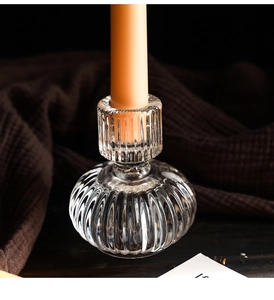 Close-up of ribbed glass candle holder with orange taper candle on a wooden table
