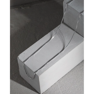 Minimalist S925 sterling silver box chain necklace draped on a grey concrete block