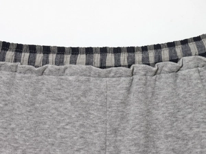 Detail of grey knit trousers featuring a black and white plaid patchwork elastic waistband