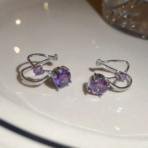Macro shot of silver ear cuff set with two purple zircon stones on white ceramic base