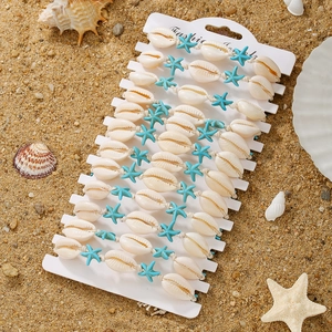Close-up of handmade shell and starfish woven bracelets set on white card and beach sand