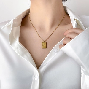 Detailed close-up of a vintage golden sunburst square pendant necklace on a white shirt