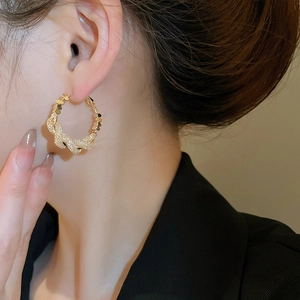 Close-up of woman wearing large gold twisted hoop earrings with shimmering zircons