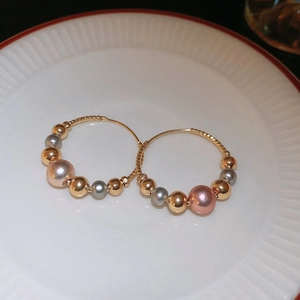 Close-up of golden twist hoop earrings with pink, grey, and gold beads on white porcelain