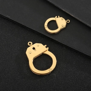 Detailed view of two gold-colored handcuff shaped metal pendants on black background