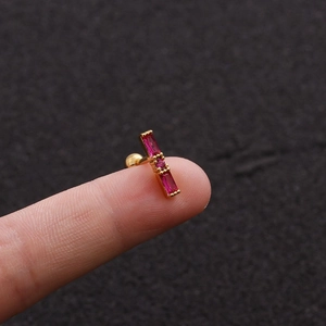 Macro shot of gold-plated stud earrings with rectangular red zircons held on a finger