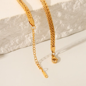 Detail view of gold stainless steel wheat chain with lobster clasp on white marble stone