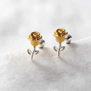 Detail of two-tone rose stud earrings with gold flower and silver stem on marble