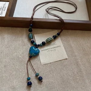 Collier ethnique avec pendentif cœur en céramique bleue et pompon sur lin beige