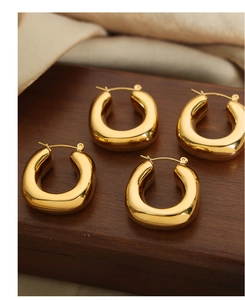 Detailed close-up of chunky gold U-shaped hoop earrings on elegant wooden stand
