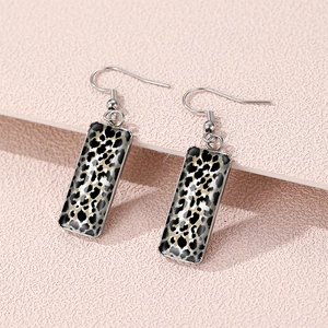 Detail shot of leopard print rectangular drop earrings on a textured pink surface