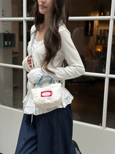 Detail of quilted cloud-texture mini crossbody bag with blue denim handle and red label