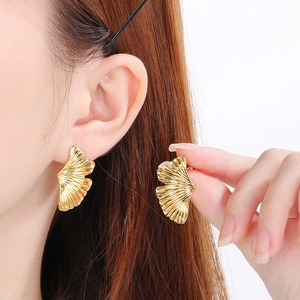 Detailed close-up of 18K gold plated brushed metal ginkgo leaf earrings worn on model