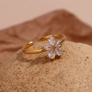 Macro shot of gold floral open ring with zircon petals on a textured stone base